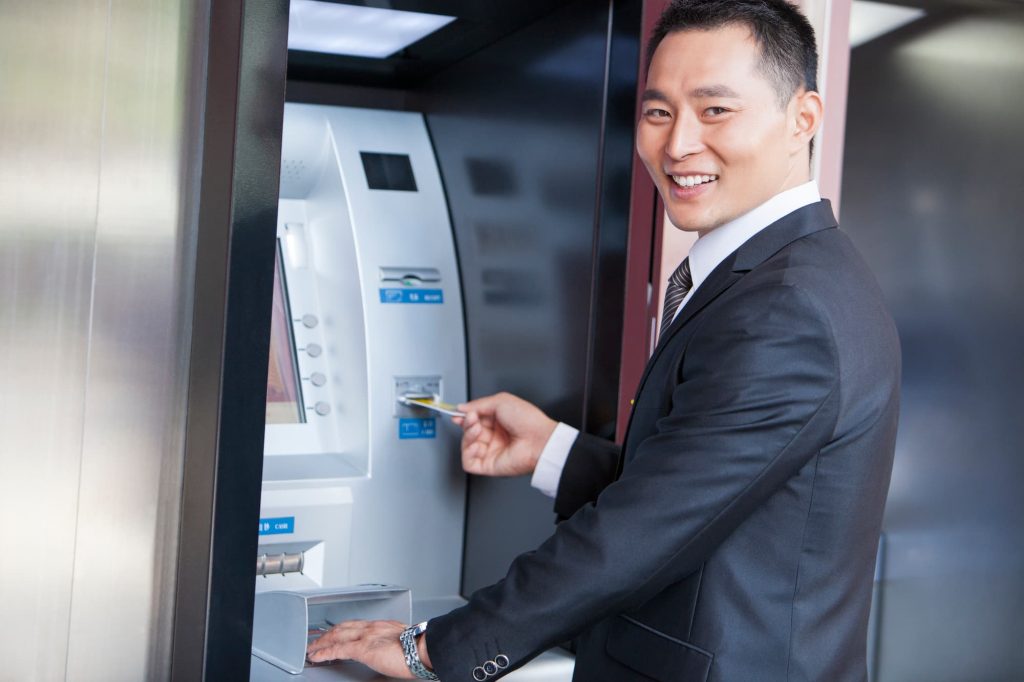 Smiling businessman using atm with bank card.